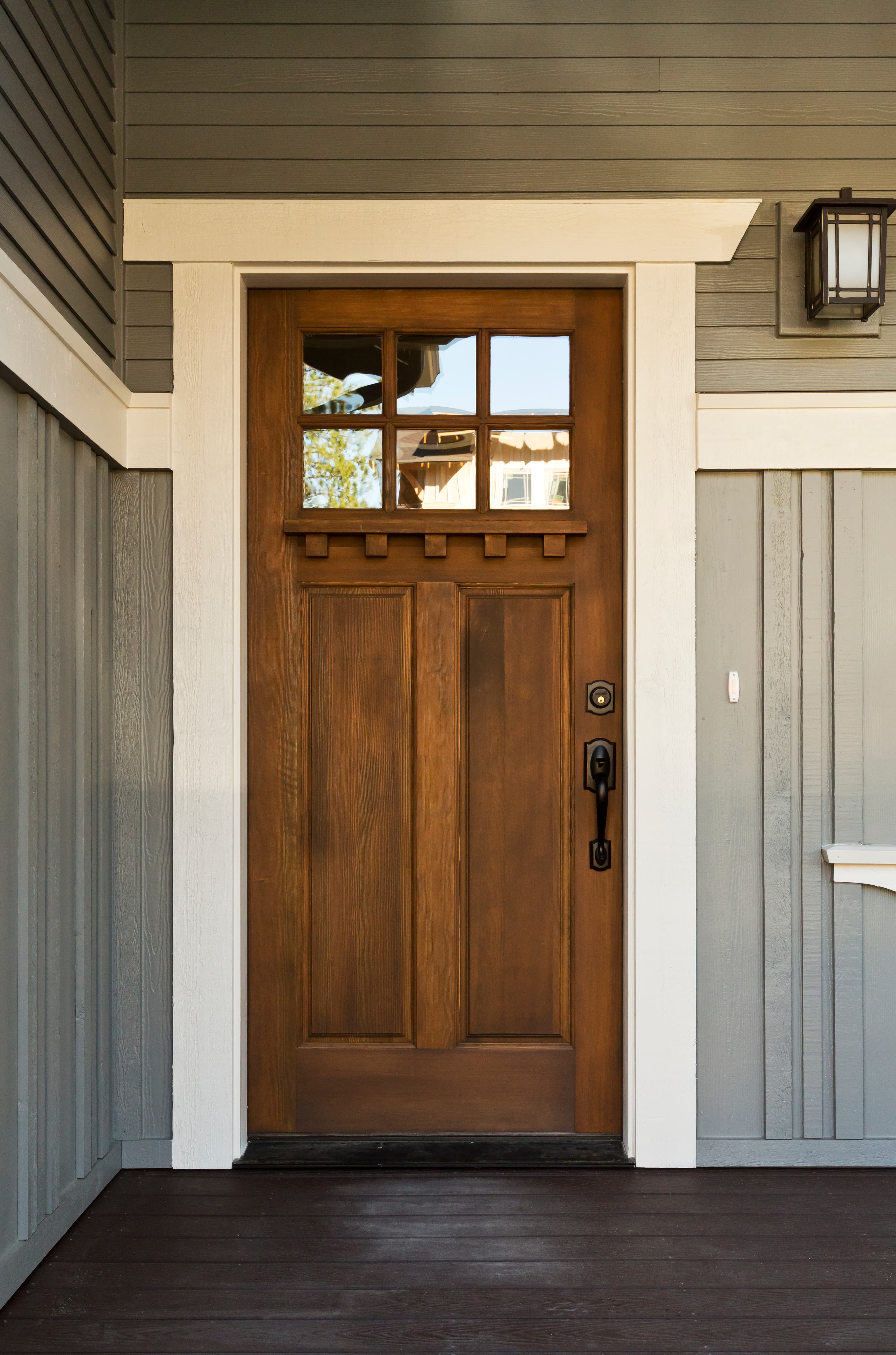 Wood craftsman entry door with iron hardware on a covered porch